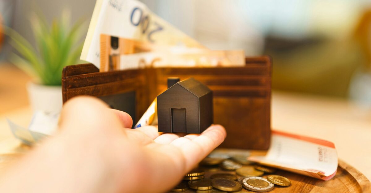 A person holding a small house and some money