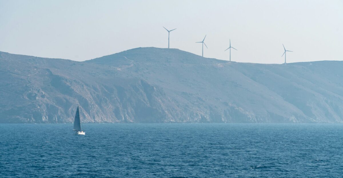 A sailboat glides past wind turbines on a hill