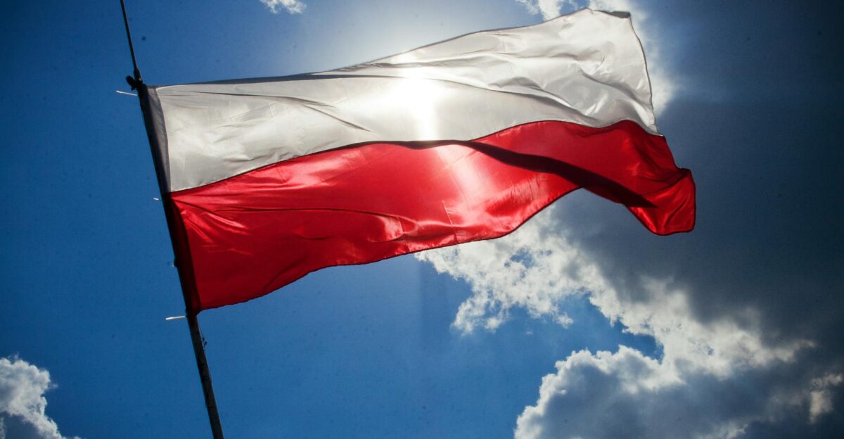 A Polish flag flutters against a bright blue sky with clouds symbolizing national pride
