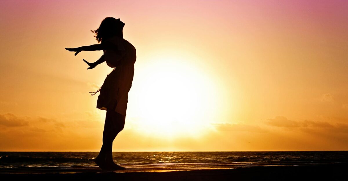 Silhouette of a woman at the beach with arms outstretched against a vibrant sunset backdrop