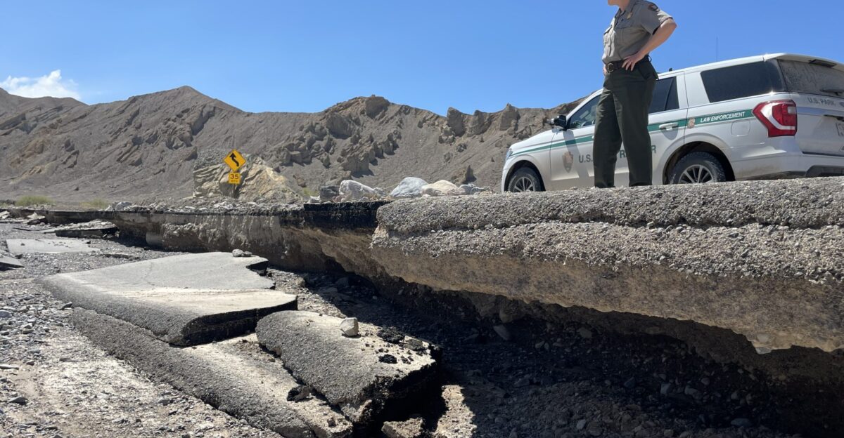 Side view of an undercut road with pavement which has fallen into the wash below and a ranger standing above on solid ground with a ranger vehicle and brown desert hills in the background A ranger looks at damage along CA 190 in Death Valley National Park Keywords Hurricane Hilary
