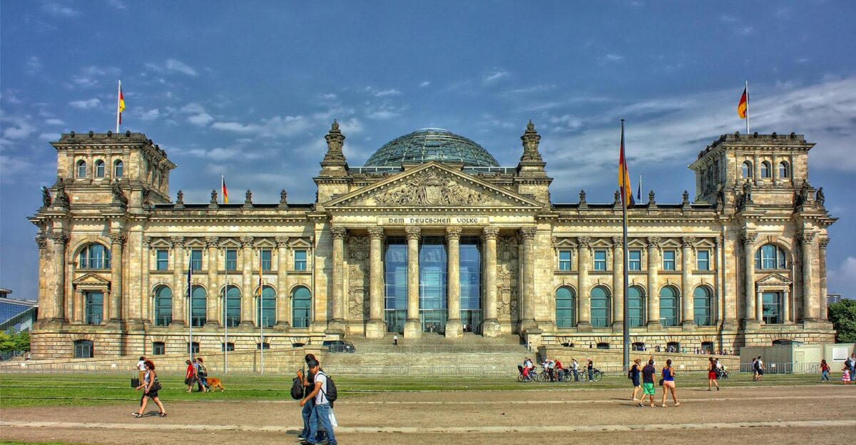 Front view of the Reichstag Building in Berlin with people and flags under a bright sky