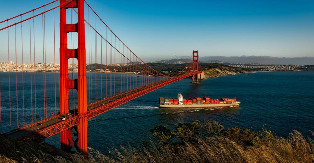 Golden Gate Bridge arches over San Francisco Bay as a cargo ship passes beneath during sunset