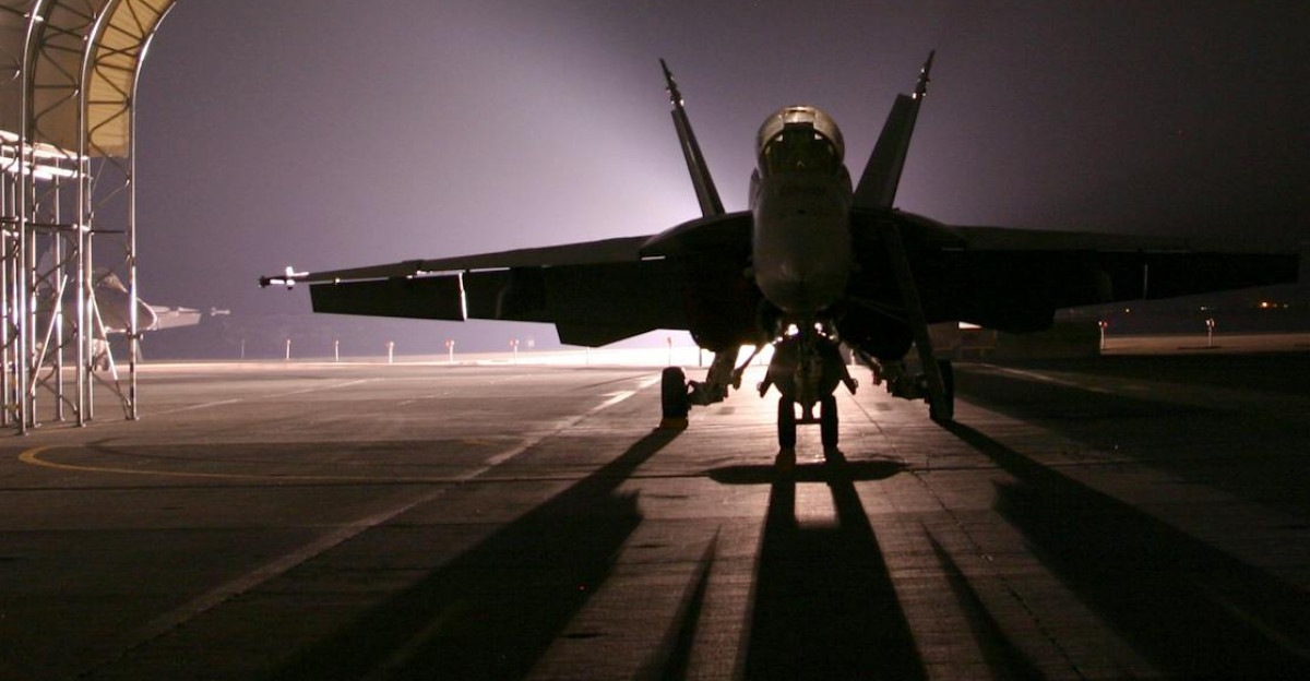Silhouetted fighter jet in an illuminated hangar at night creates a dramatic scene