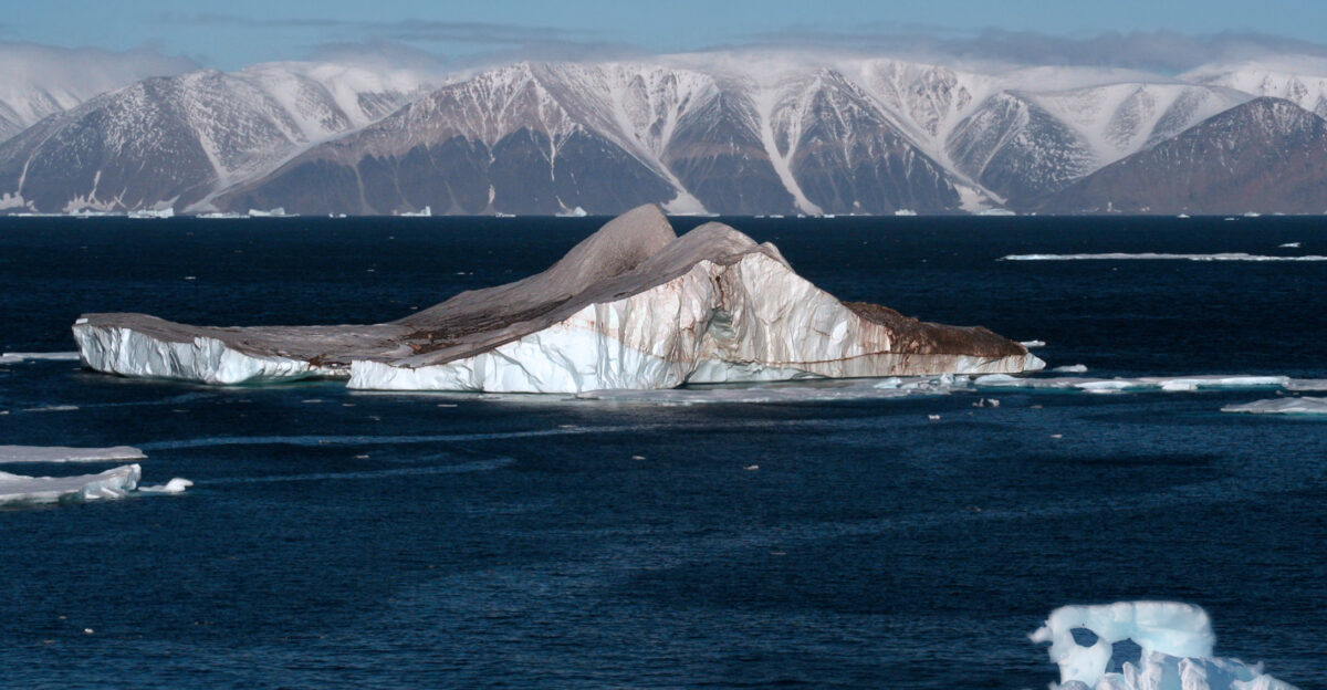 Icebergs in the High Arctic The image was sent to a glaciologist Thomas Allen Neumann It is what he wrote about the coloration of the iceberg It s too red to be oxidation like blood falls in Taylor Valley The debris loading isn t particularly extensive the apparent slip plane is interesting or perhaps a former water channel but the color is usual Red algae would be a good guess Two colleagues have also seen your photo and suggested the majority of the debris was from ah biological activity Specifically they suggested the reddish appearance may be due to walrus excrement - another example is here 1 That would explain the color but perhaps not the discoloration along the band through the ice berg The part of his email to me was added with his permission