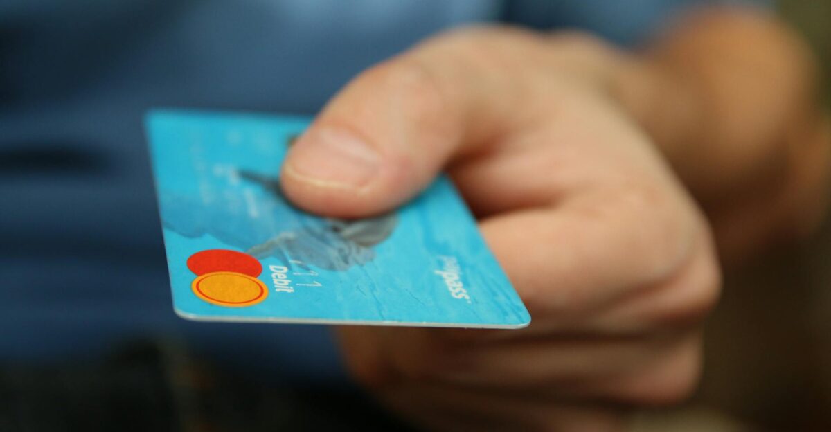 A close-up shot of a hand offering a blue debit card for payment