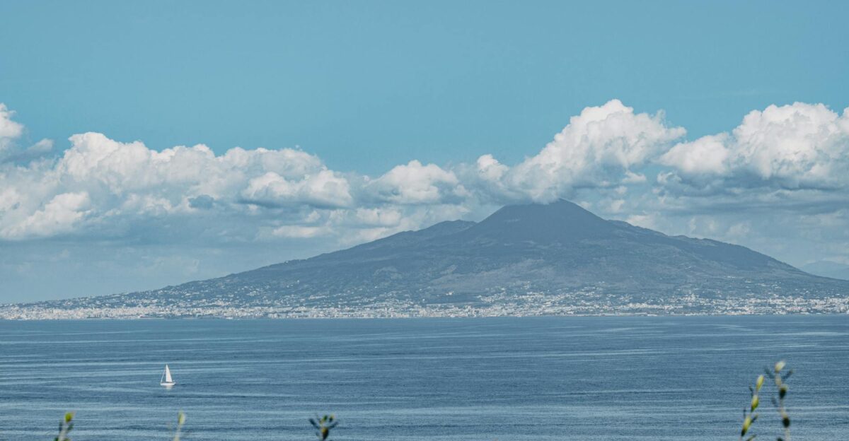 Scenic view of Mount Vesuvius with a sailboat on the Bay of Naples under a clear blue sky