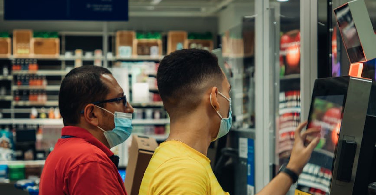 Two men wearing masks using a self-checkout machine in a grocery store