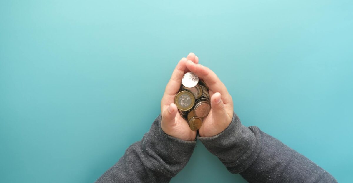 Two hands holding a stack of coins against a blue background symbolizing savings or financial security