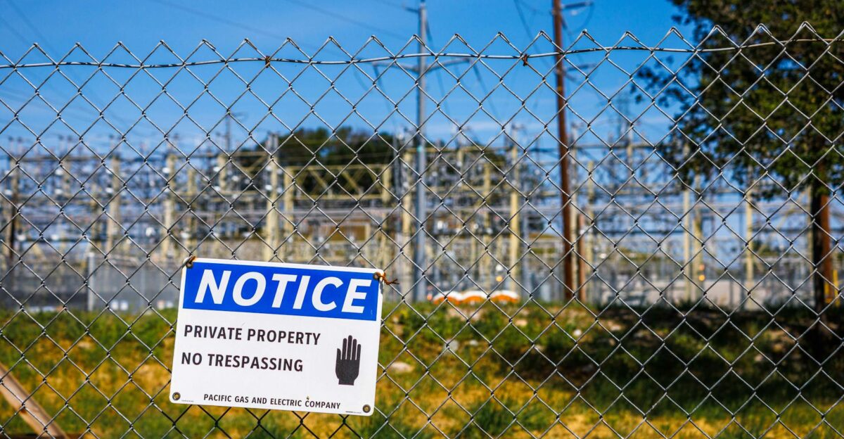 Chain link fence with a private property no trespassing notice sign and electrical infrastructure in the background