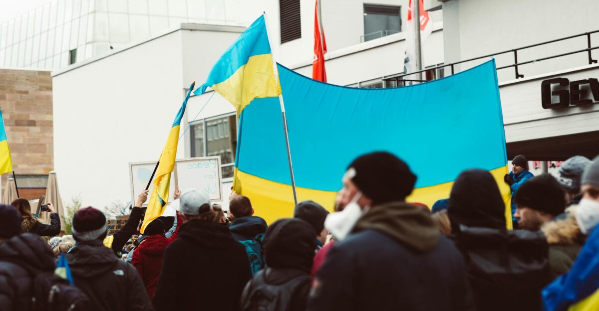 A large group of people rally outdoors holding Ukrainian flags during a peace protest