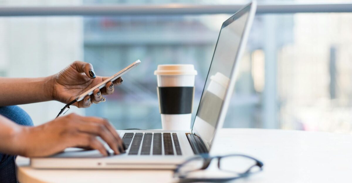 Close-up of hands using a laptop and phone with coffee on a modern office desk