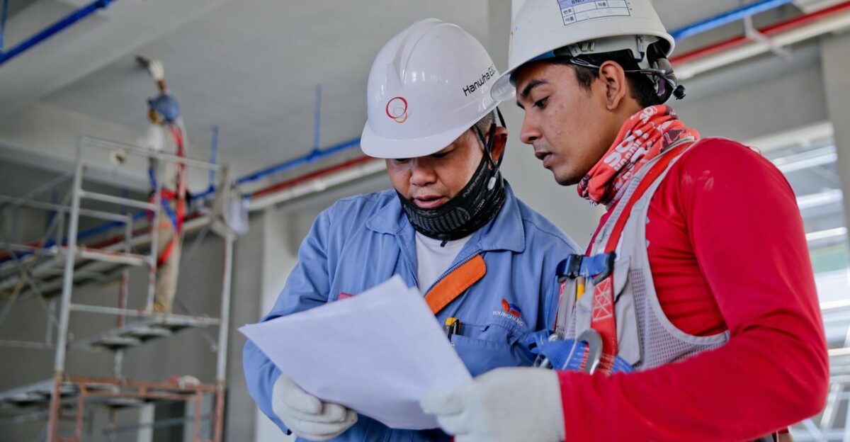 Two engineers in safety helmets reviewing construction plans at a worksite