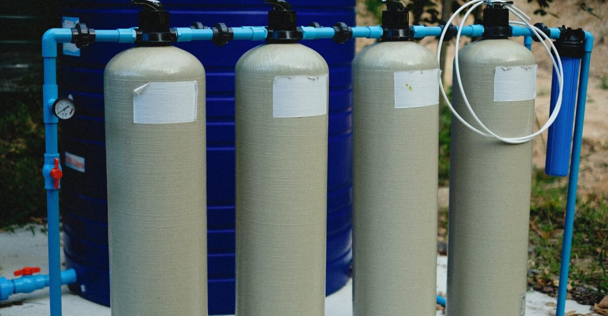 Four beige tanks in an outdoor water treatment setup with blue piping