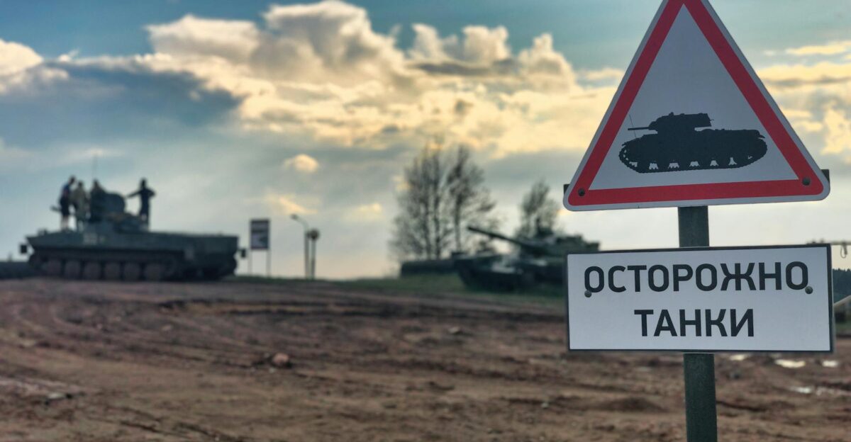 Military tanks in Belarus with a warning sign for caution on dirt road