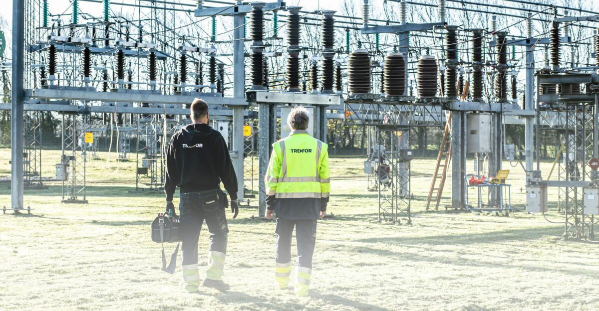 Two workers inspect an outdoor electrical substation emphasizing safety and maintenance