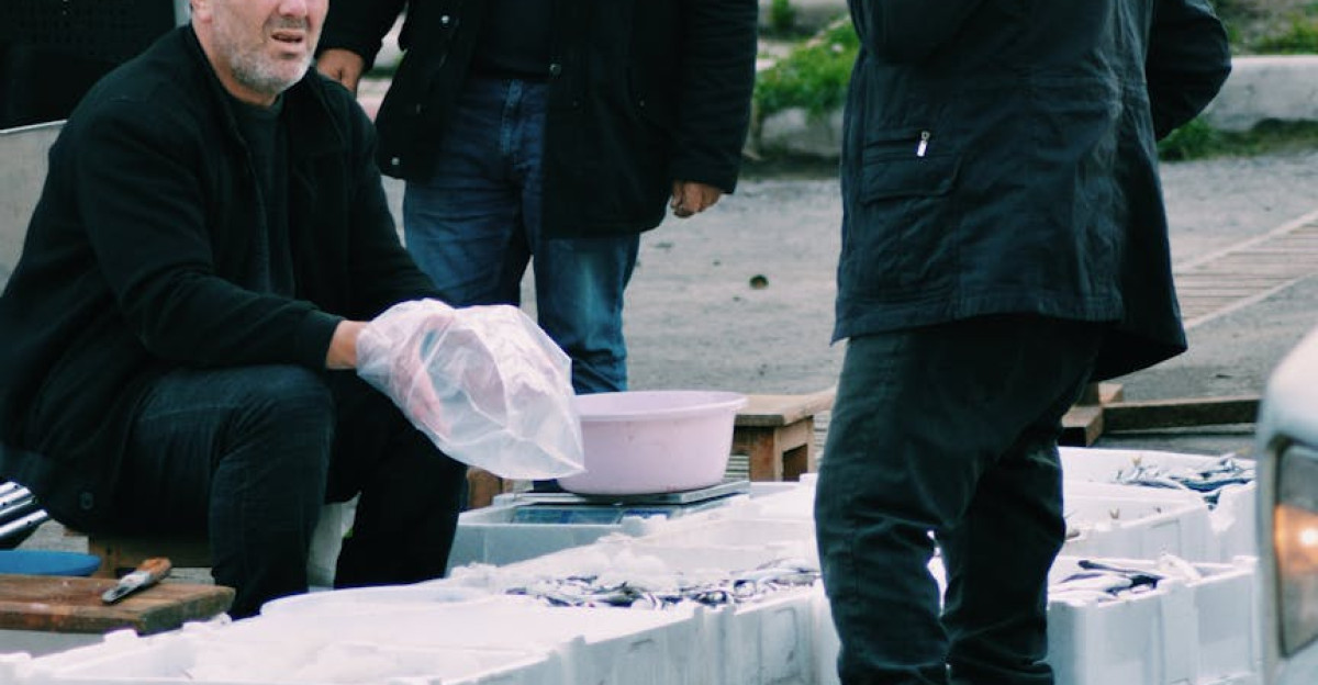 Three men at an outdoor market selling goods under umbrellas engaging in business