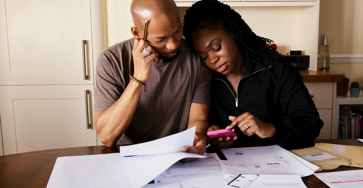 A couple sits at a table managing domestic finances evaluating documents and using a smartphone