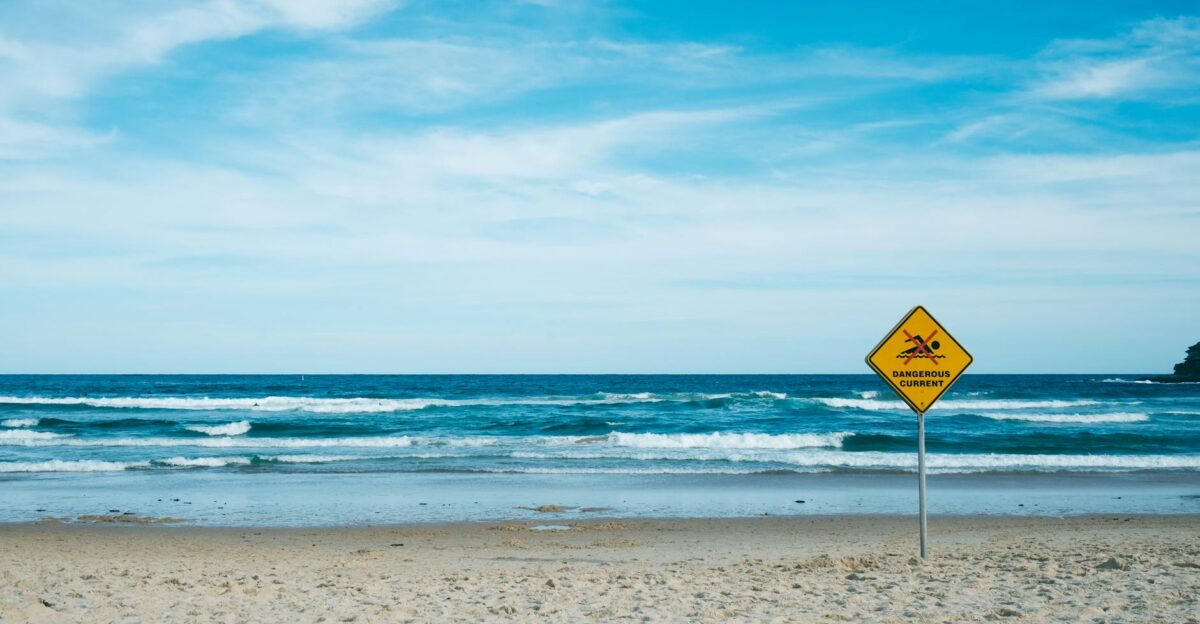 A tranquil beach scene with a warning sign about dangerous currents by the blue sea