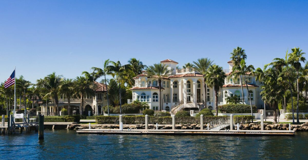 Elegant waterfront mansion with palm trees and clear blue sky showcasing opulence and coastal vibe