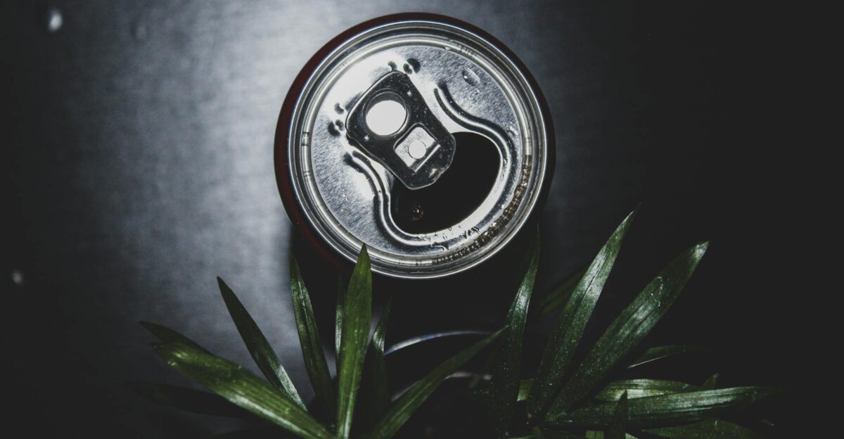 Close-up image of an opened metal can against a dark background with plant leaves in view