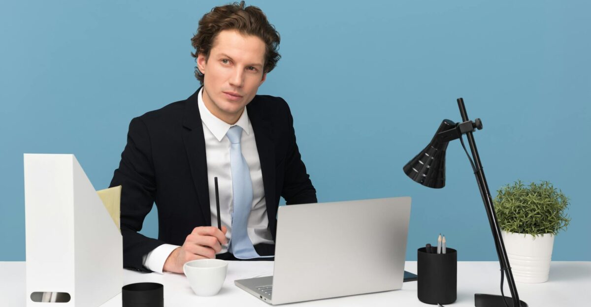 A focused businessman in a suit works at his tidy desk with a laptop plant and lamp