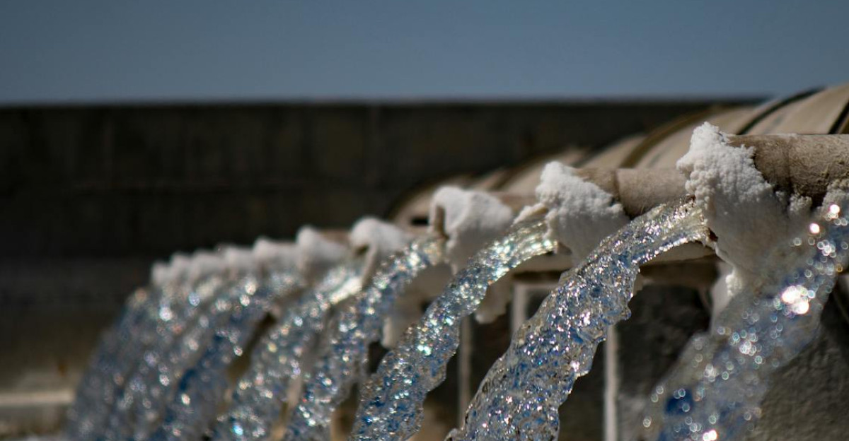 Close-up view of water flowing from industrial pipes against a clear blue sky