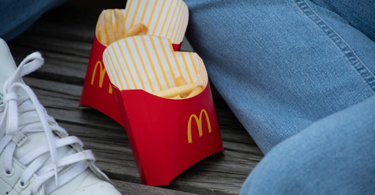 Two red cartons of McDonald s French fries between jeans and sneakers on a wooden surface