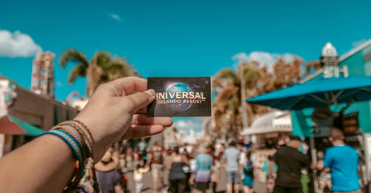 A hand holding a Universal Orlando Resort ticket in a bustling theme park setting