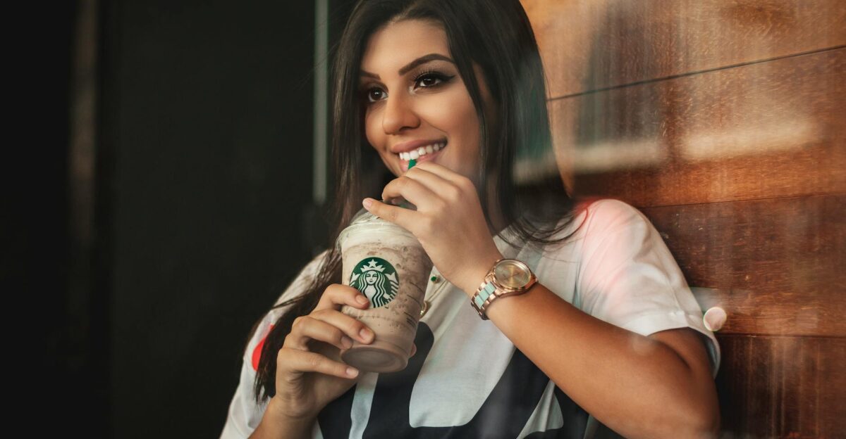 Young woman smiling while sipping a Starbucks iced coffee indoors
