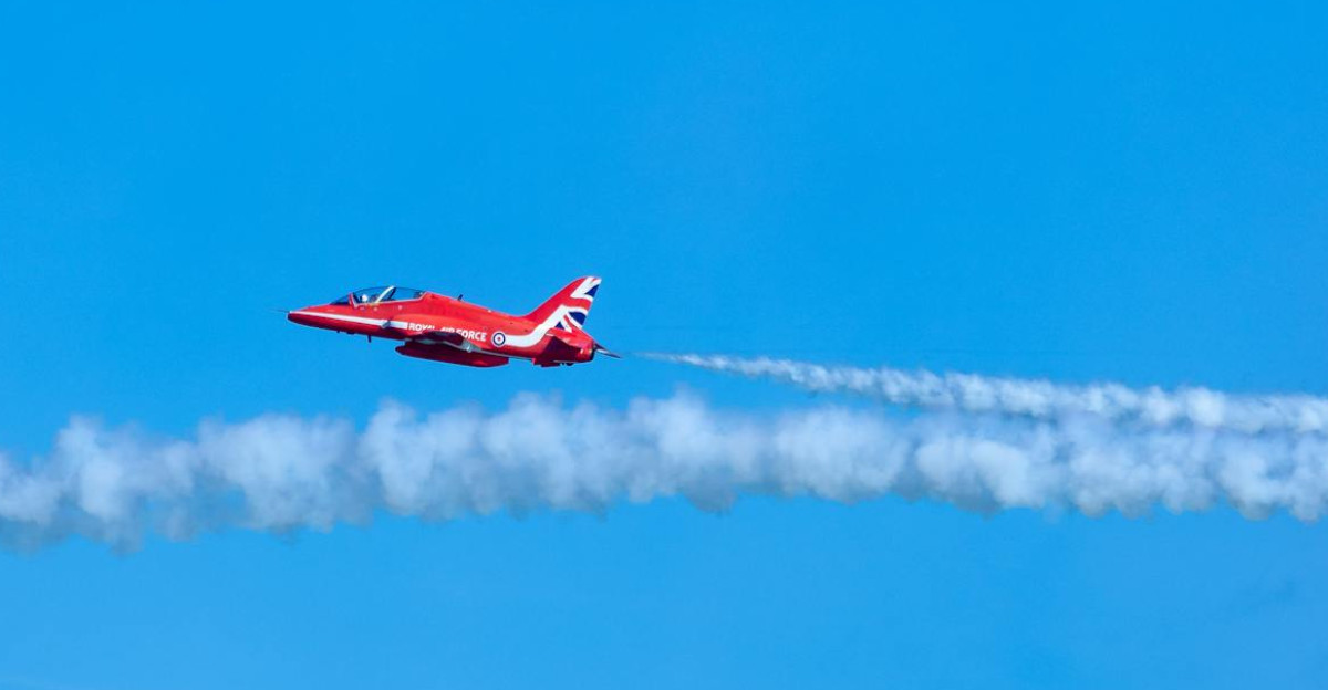 Red Arrows aircraft flying through clear blue sky leaving trails of smoke