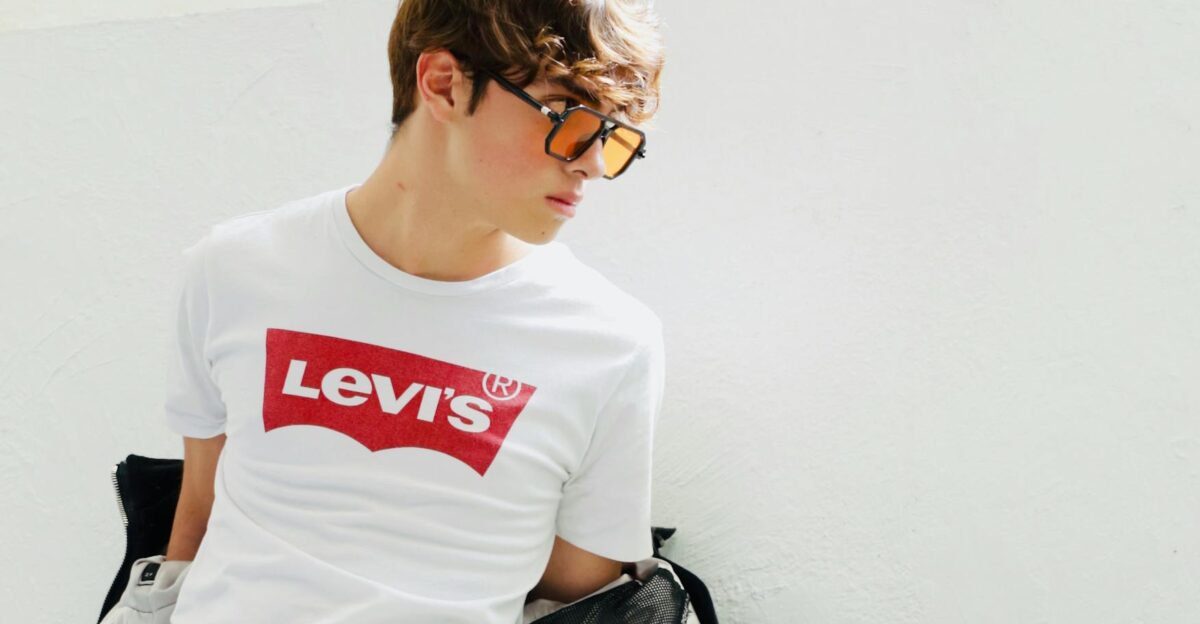 Stylish young man wearing Levi s t-shirt with sunglasses against a white background