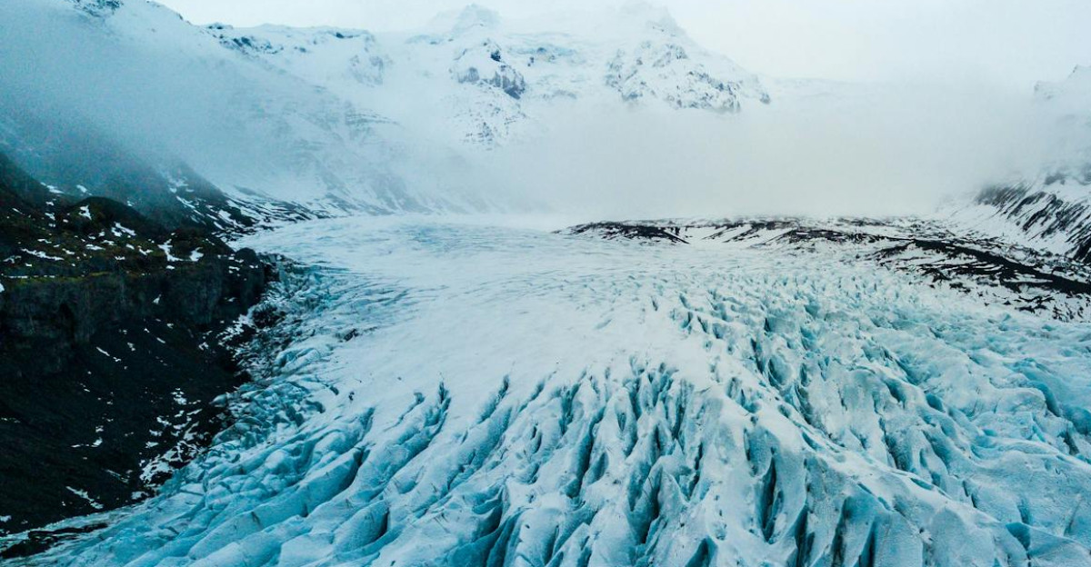 A breathtaking aerial shot of a vast icy glacier surrounded by snow-capped mountains in winter