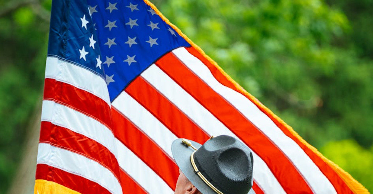 Military officer holding the American flag with vibrant greenery in the background