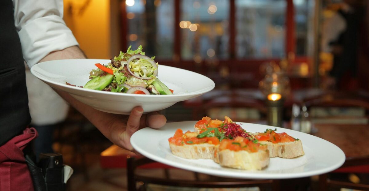 A waiter serves a fresh salad and hors d oeuvres in a cozy restaurant setting