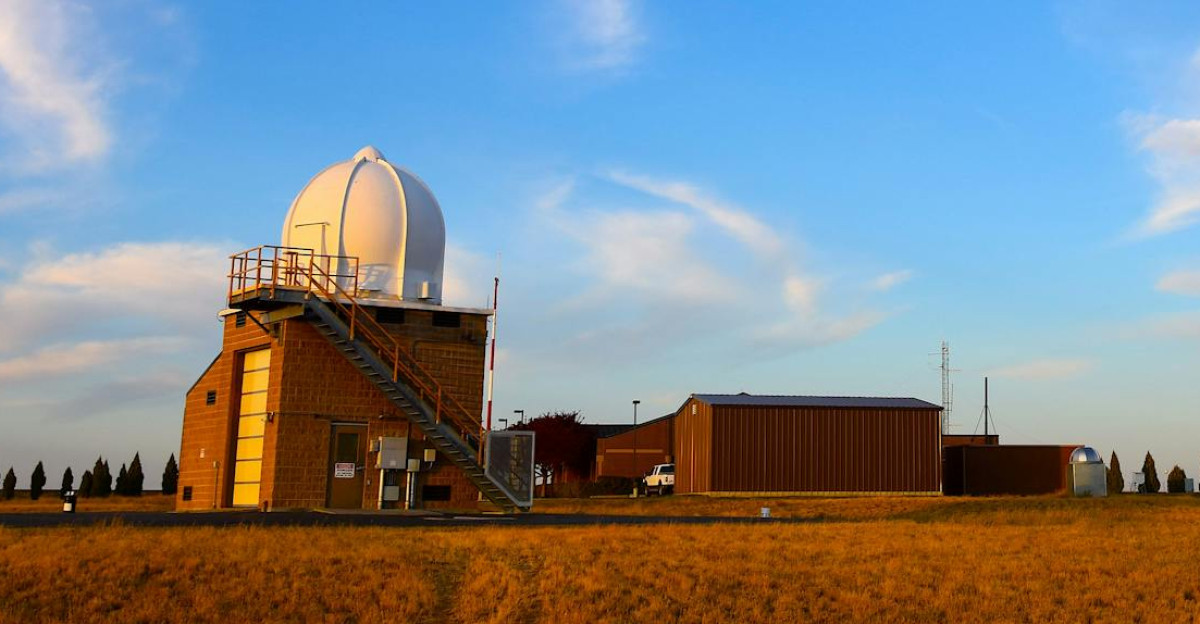 Weather radar station set in a field with a clear blue sky and scattered clouds showcasing meteorological technology