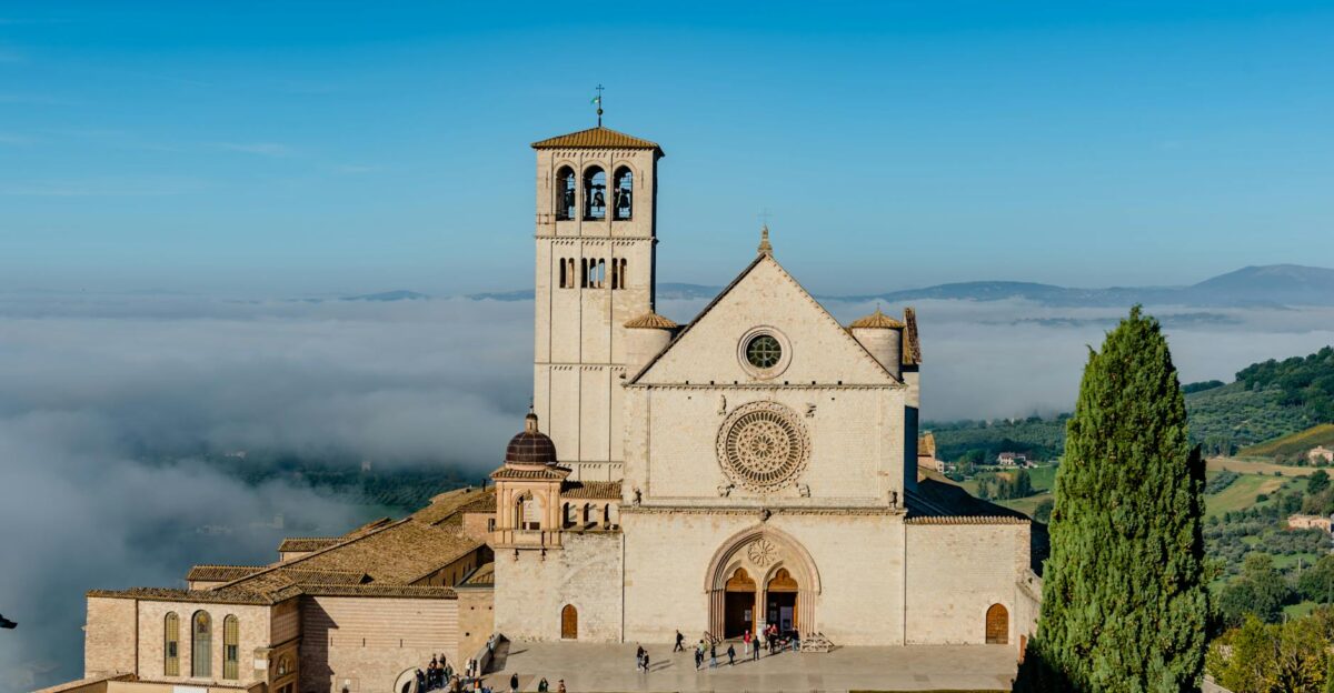 Basilica di San Francesco in Assisi Italy with misty hill views and vibrant blue sky