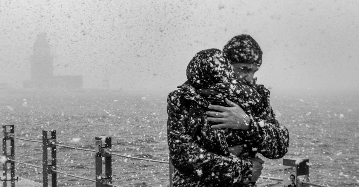 A moving black and white photo of a heartfelt embrace during a snowfall at the waterfront