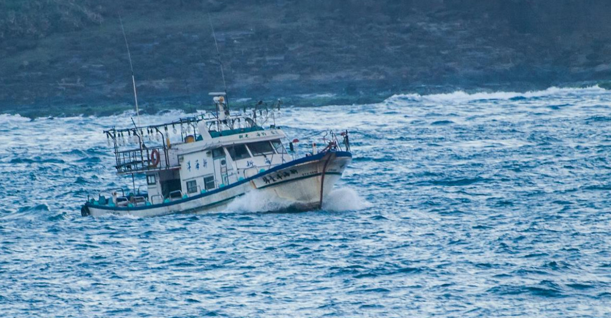 A fishing boat sails through choppy ocean waves near a rocky coastline capturing maritime adventure