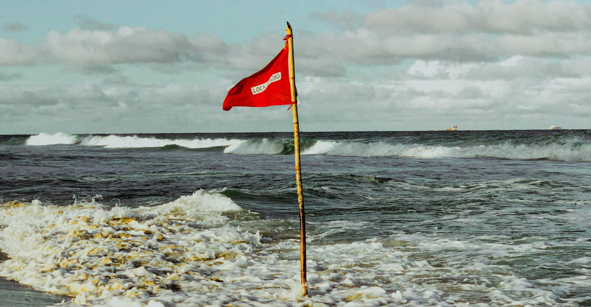 Red flag on a beach indicating dangerous swimming conditions amid strong waves in Brazil's Santa Catarina coast.