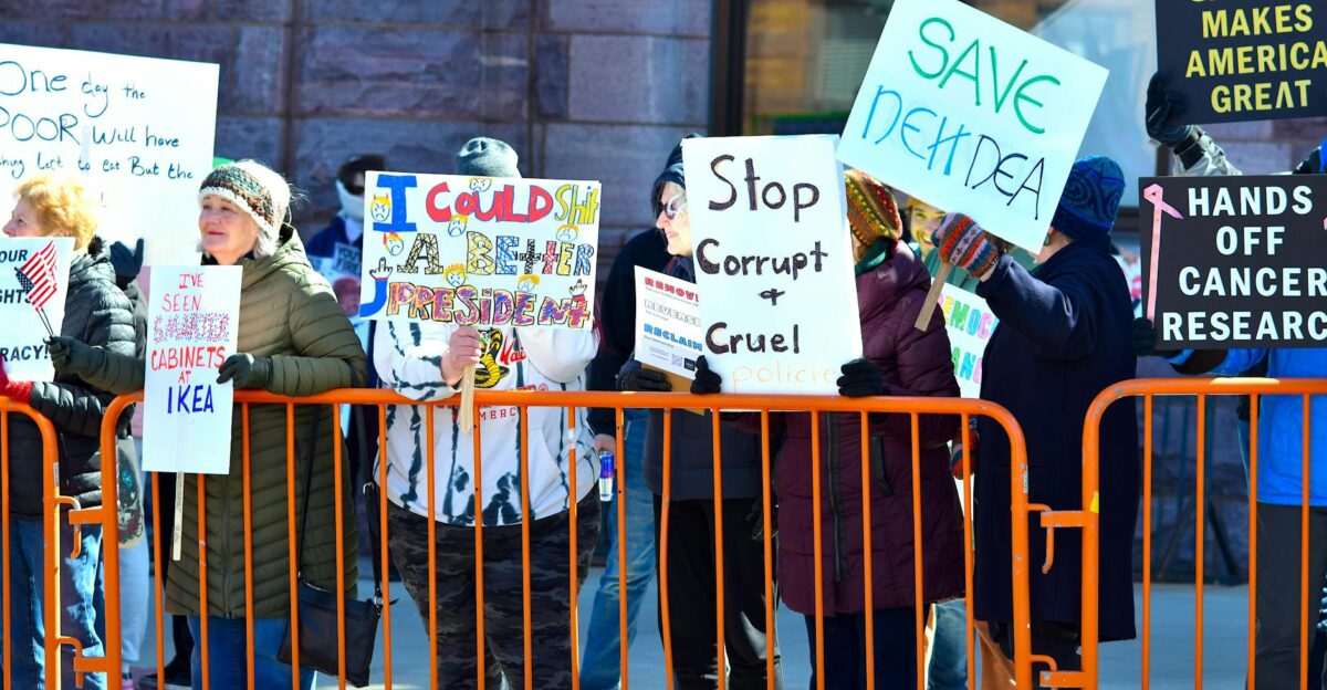 A group of people holding signs in a street protest expressing dissent against political policies