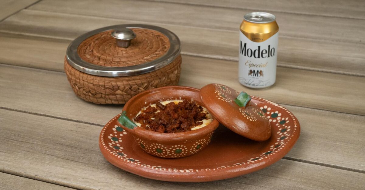 Traditional Mexican queso fundido with chorizo served alongside a Modelo beer on a rustic wooden table