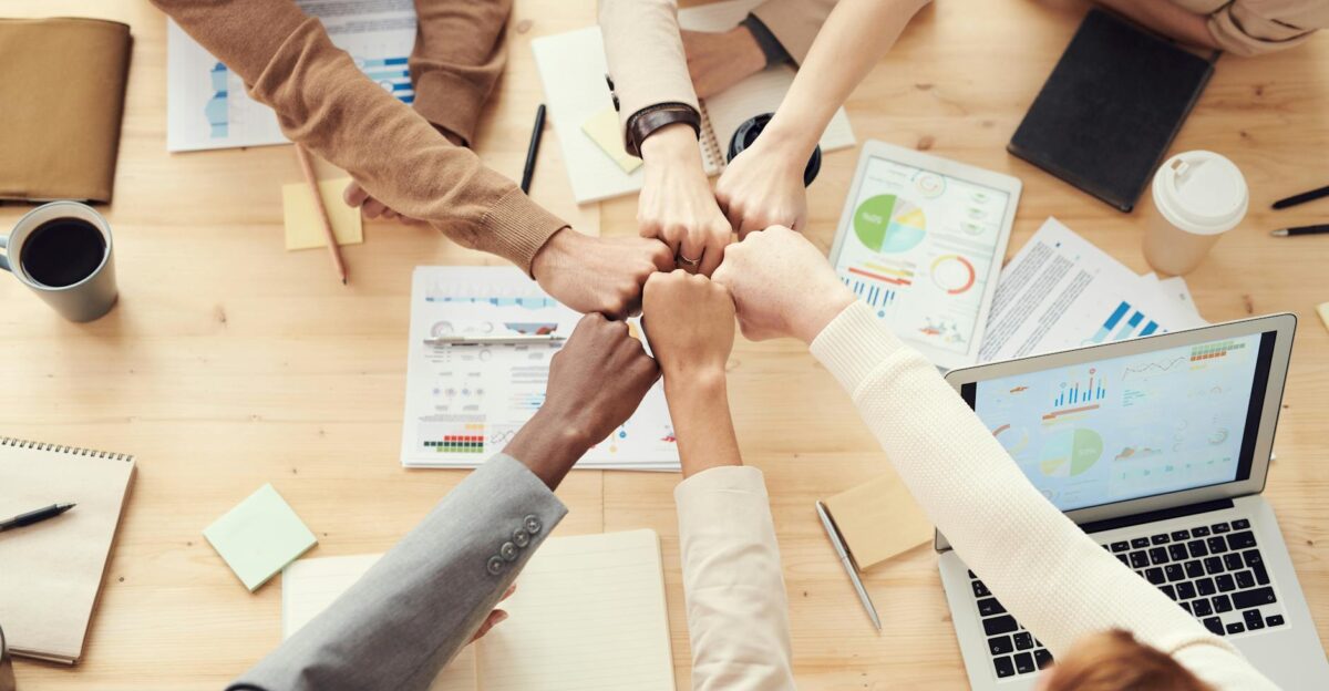 Top view of a diverse team fist bumping over a meeting table with paperwork and laptops symbolizing teamwork