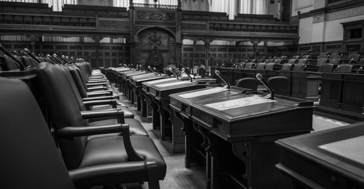 Black and white photo of a traditional legislative assembly chamber featuring empty seats and desks
