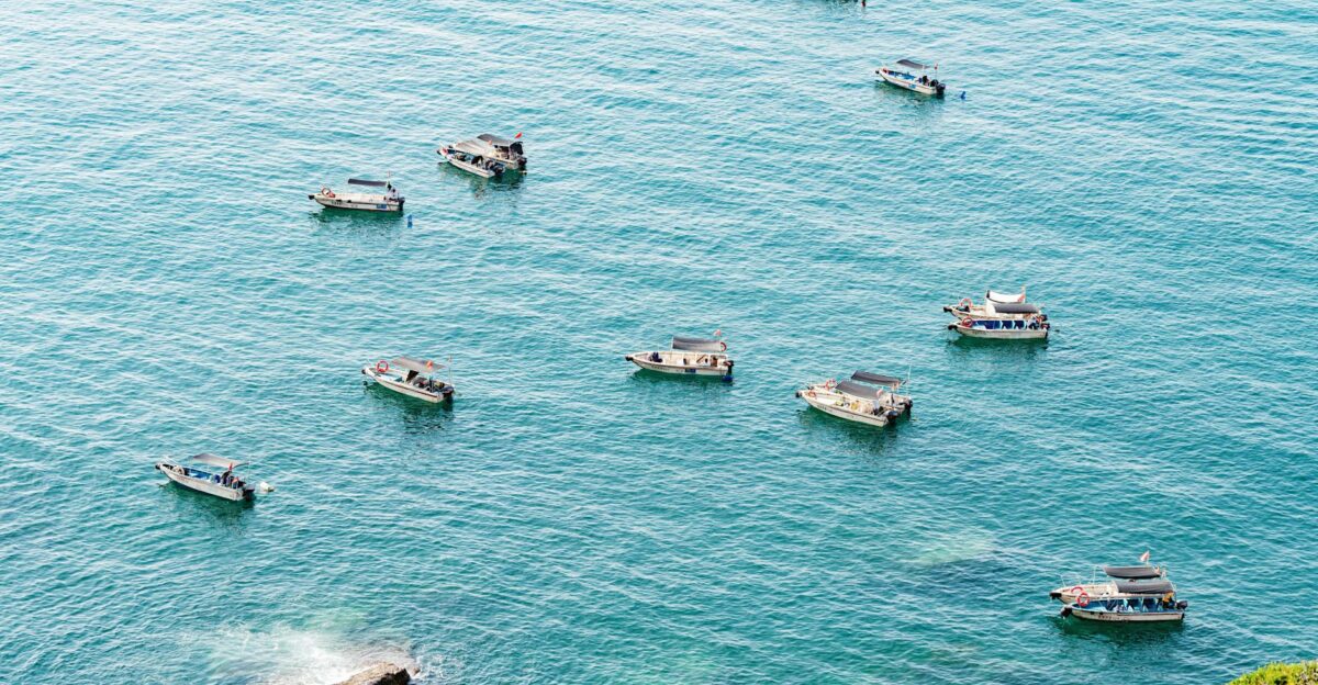 Aerial view of multiple boats floating on calm turquoise sea under bright daylight