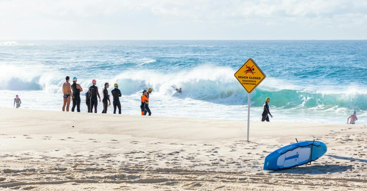Group of surfers on a beach with a Beach Closed sign and waves in the background
