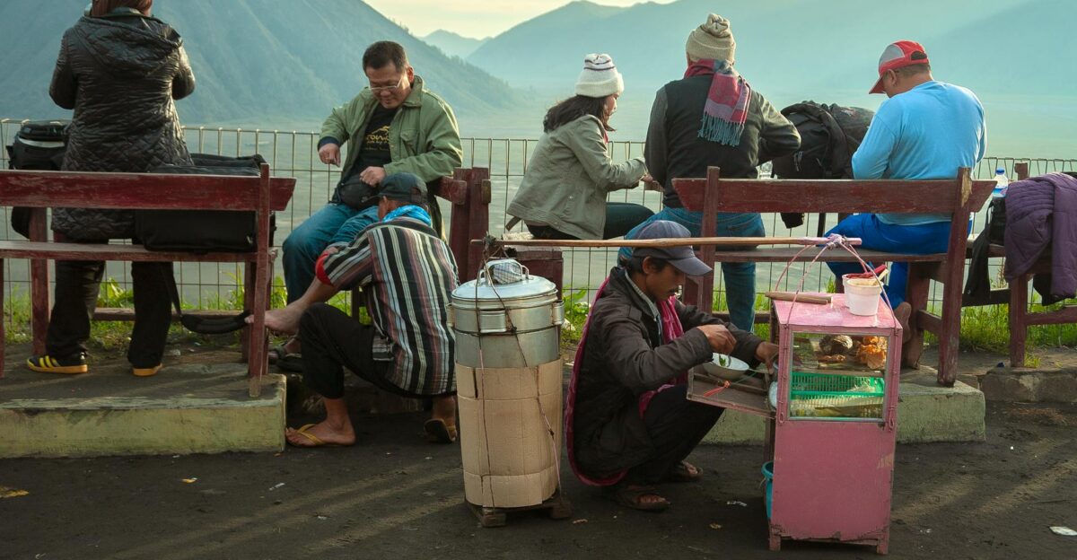 A street vendor serves food to tourists near a scenic mountain backdrop