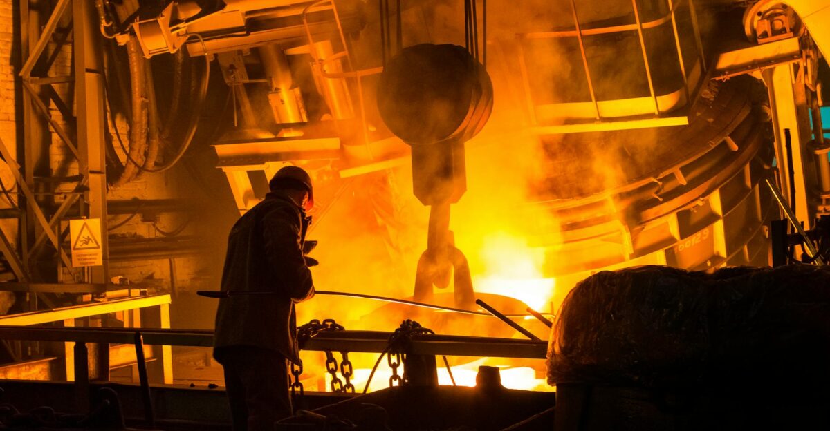 A worker operates machinery in a factory with molten metal and intense flames