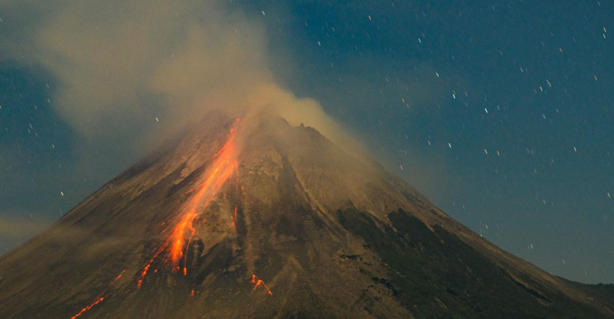 A nighttime view of a volcanic eruption with glowing lava and a starry sky