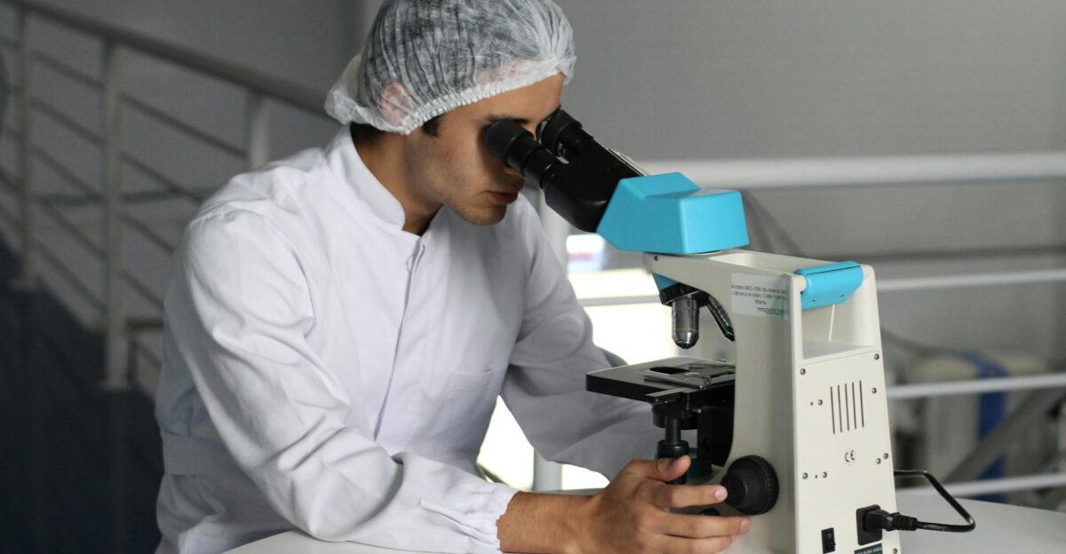 Scientist in a lab coat using a microscope to conduct research focusing on healthcare improvements